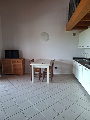 A kitchen with a dining table, chairs, a television, cabinets, and a tiled floor. - Casa Manerba, near Romantica Beach (Lombardia)