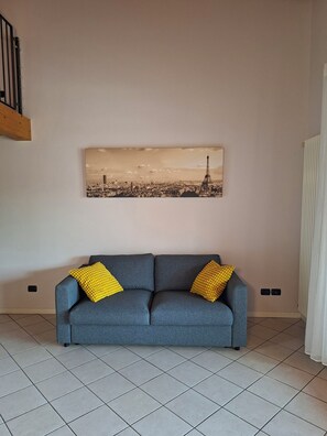 A grey sofa with yellow cushions, a cityscape painting above it, and a radiator on the wall. - Casa Manerba, near Romantica Beach (Lombardia)