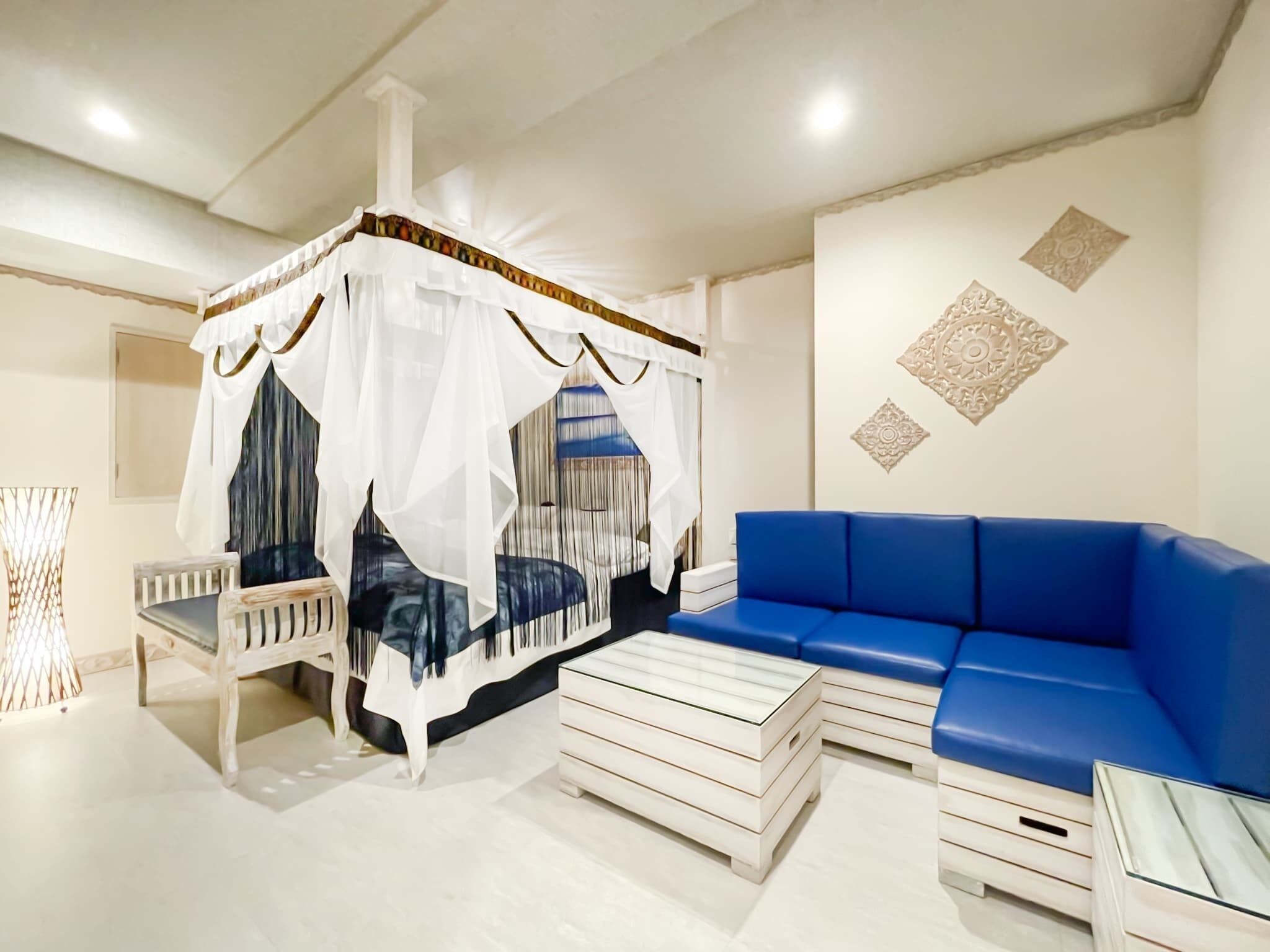 A bedroom with a canopy bed, a blue sofa, a small table, and decorative wall patterns.