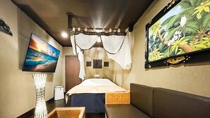 Una habitación con cama, televisión, un cuadro y un banco de fibras naturales.
