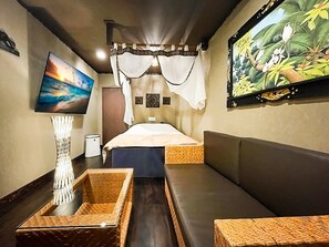 Um quarto com uma cama, uma televisão, um quadro e um banco de fibra natural.