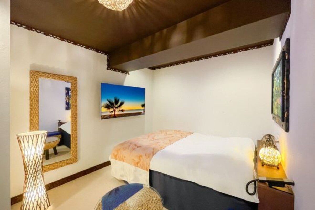 Un dormitorio con cama, lámpara de noche, espejo y un cuadro en la pared.