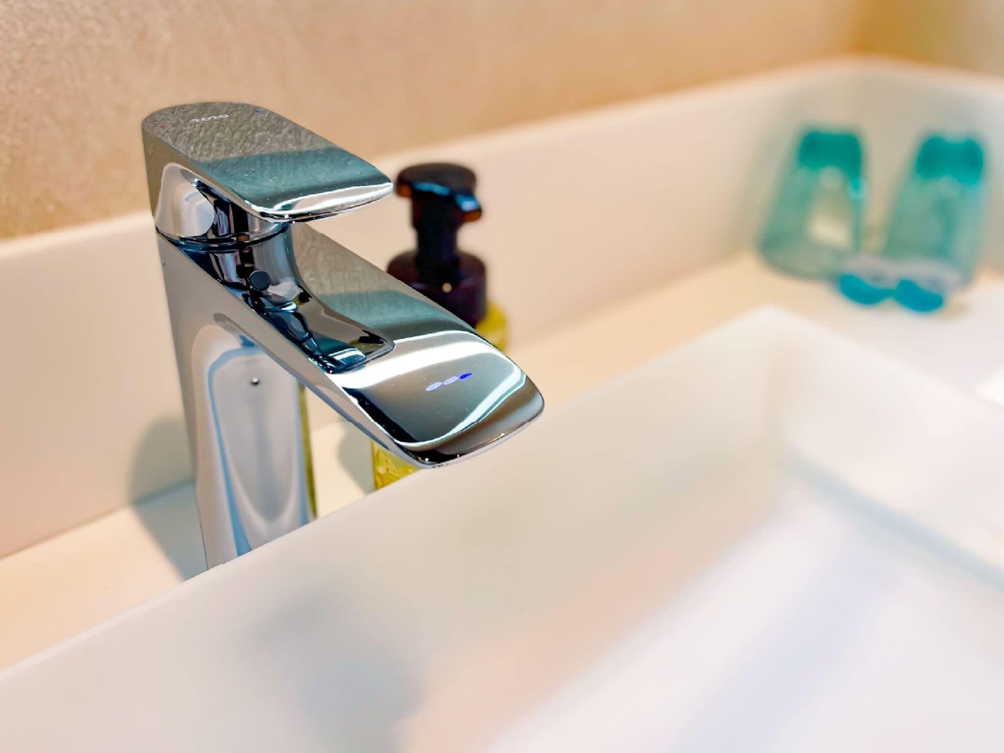 A modern bathroom with a chrome faucet, a soap dispenser, and a clear glass soap dish.
