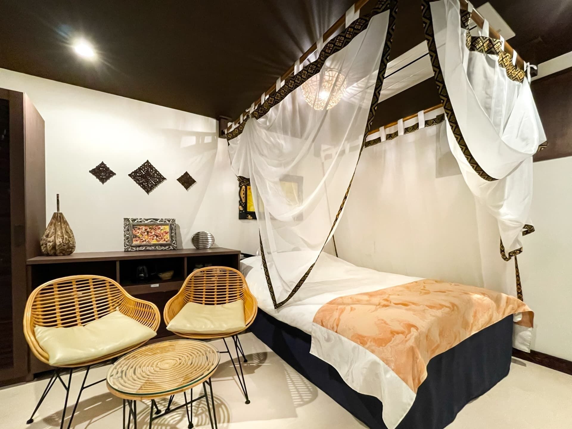 A room with a bed, two chairs, a small table, a decorative cabinet, and a canopy bed.