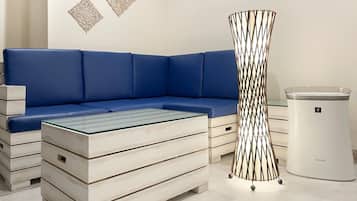 Una sala de estar moderna con un sofá seccional azul, una mesa de centro de vidrio, un bote de basura blanco y decoración en la pared.