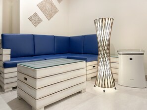Una sala de estar moderna con un sofá seccional azul, una mesa de centro de vidrio, un bote de basura blanco y decoración en la pared.