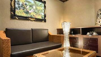 A room with a black leather sofa, a glass coffee table, a decorative vase, a wall-mounted painting, and a wooden cabinet with dishes.