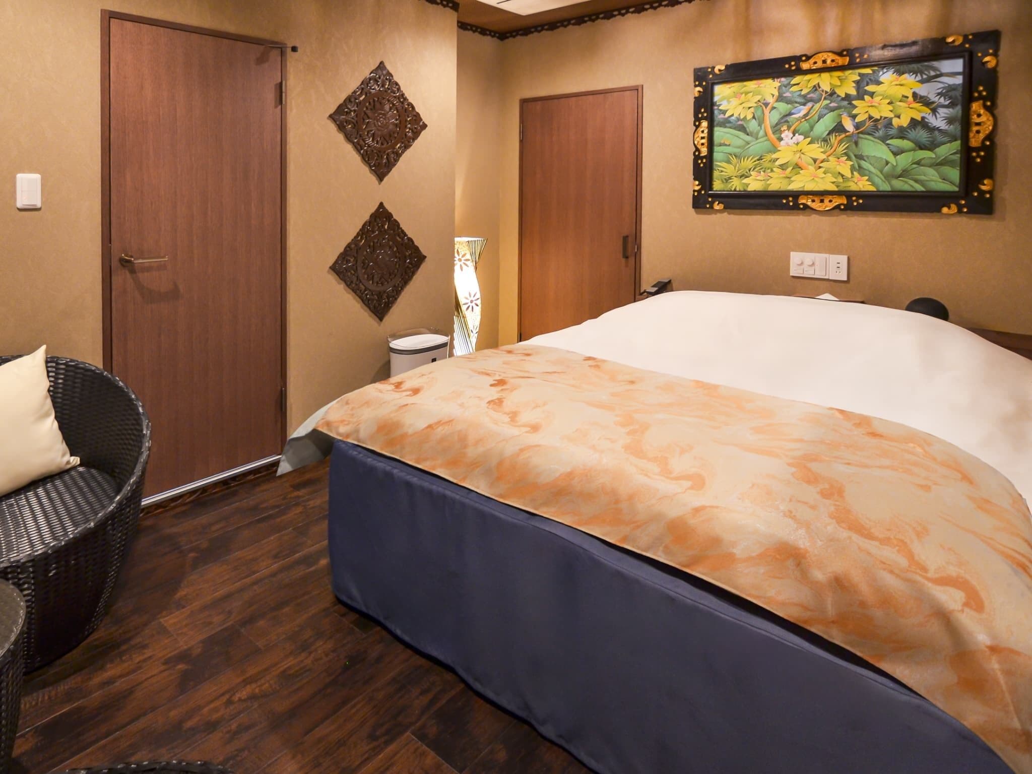 A hotel room with a large bed, two doors, a chair, and a wall-mounted painting.