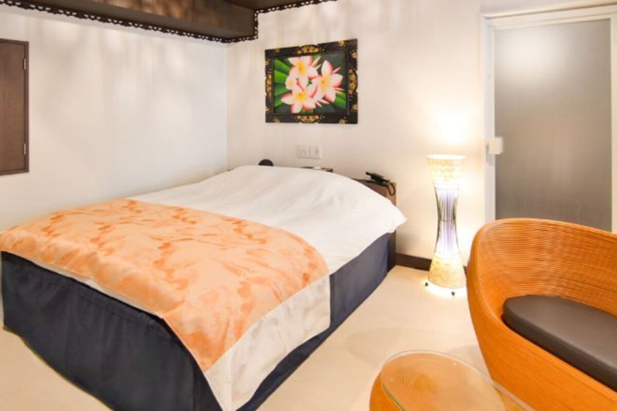 Una habitación de hotel con una cama, una silla, una lámpara y un cuadro en la pared.