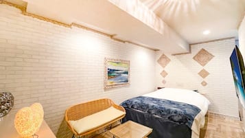 A bedroom with a bed, a chair, a table, a wall-mounted painting, and a decorative light fixture.