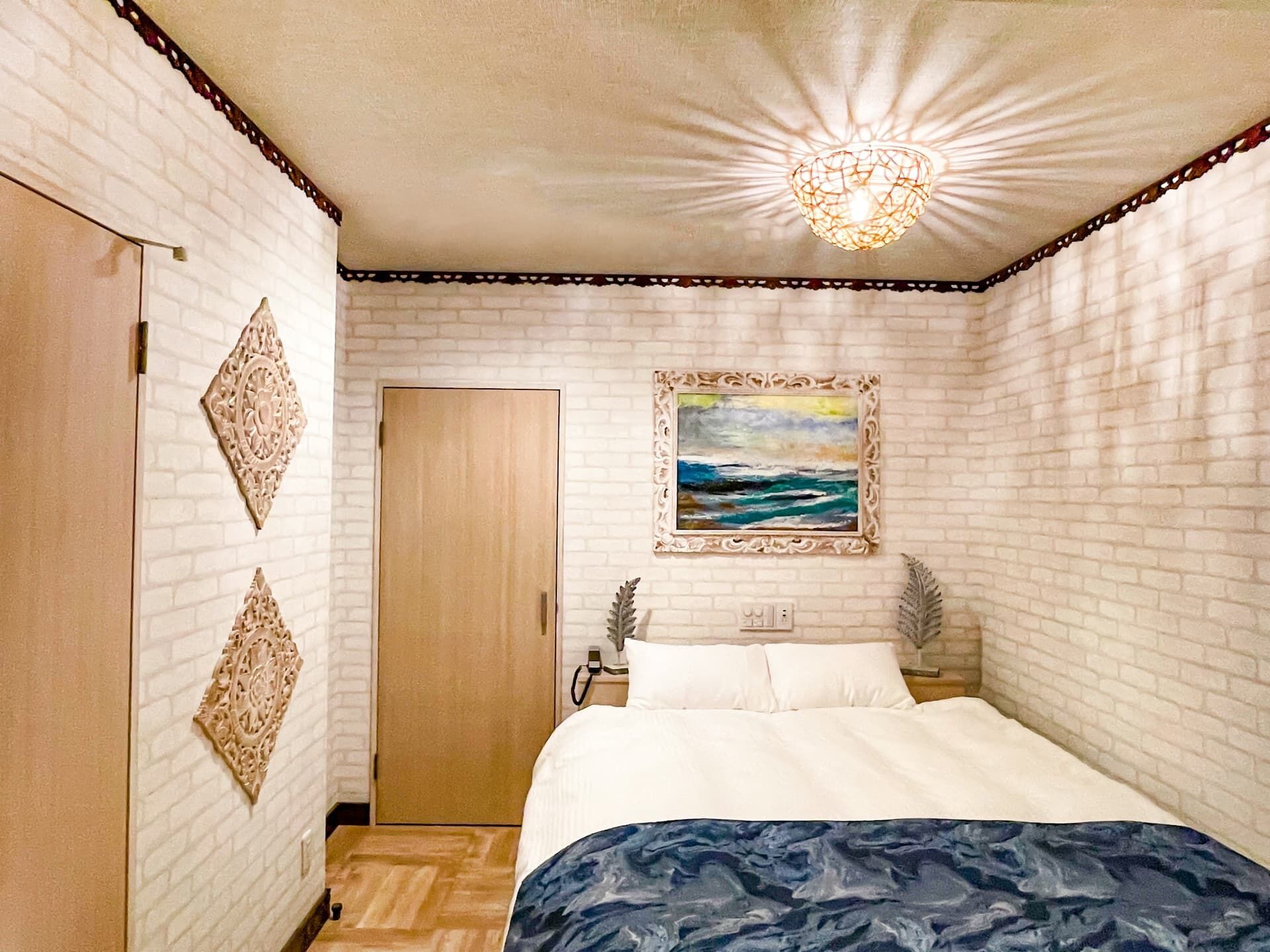 A bedroom with a bed, a painting, a wooden wardrobe, and a decorative ceiling light.