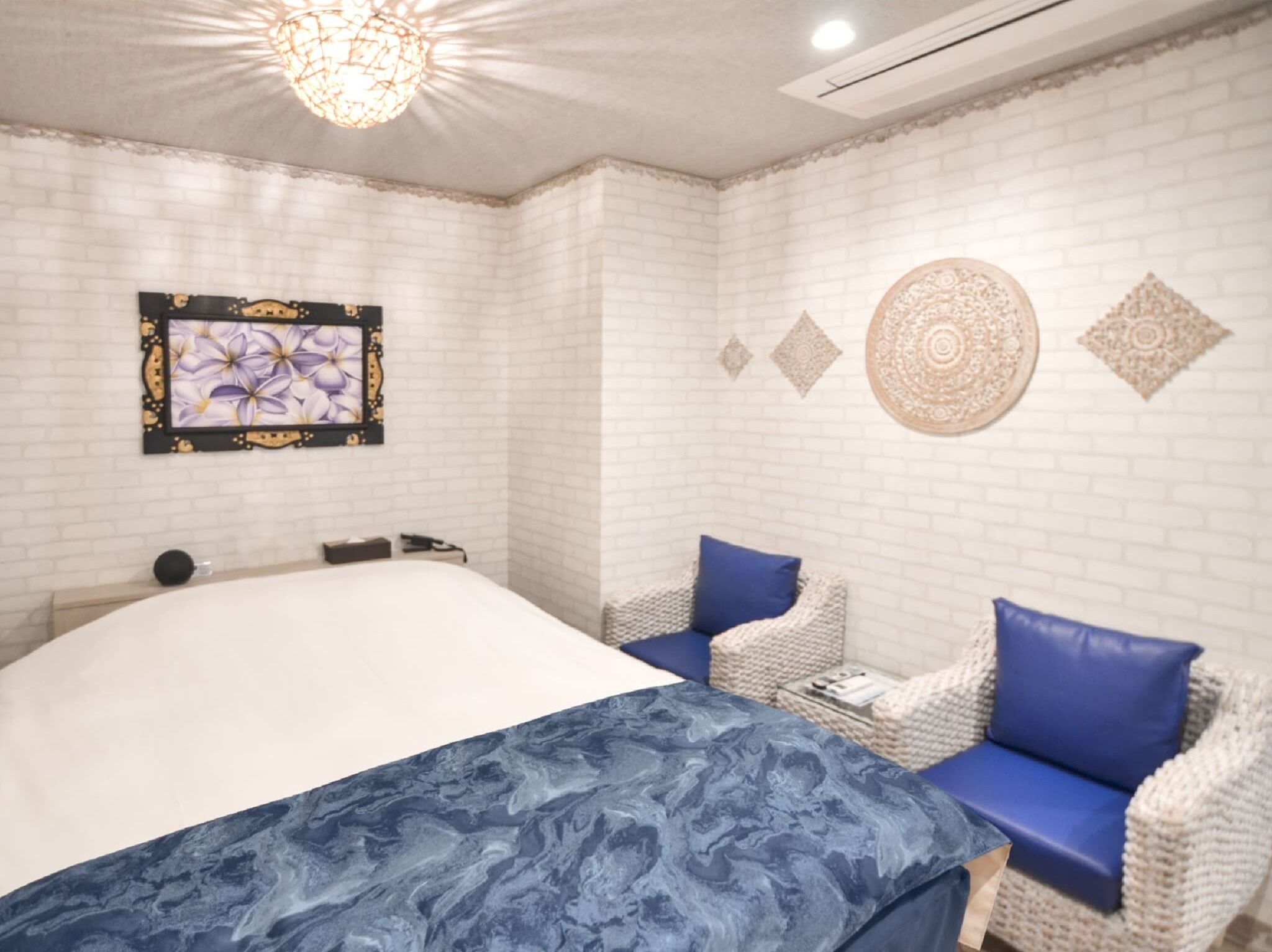 A bedroom with a bed, two chairs, a wall-mounted artwork, and decorative wall patterns.