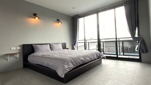 Ein modernes Schlafzimmer mit einem großen Bett, zwei Wandleuchten, einem Fenster mit Vorhängen und Balkonblick.