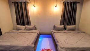 Ein Zimmer mit zwei Betten, einer zentralen Lichtleiste und einer Blumenvase.
