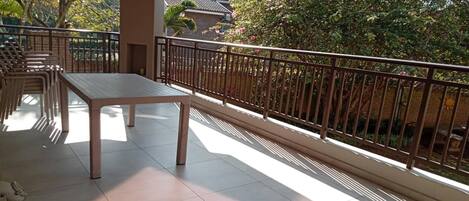 A balcony with a table and chairs, a railing, and a view of trees and a building.