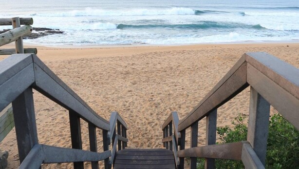 A wooden staircase leading to a sandy beach with ocean waves in the background.