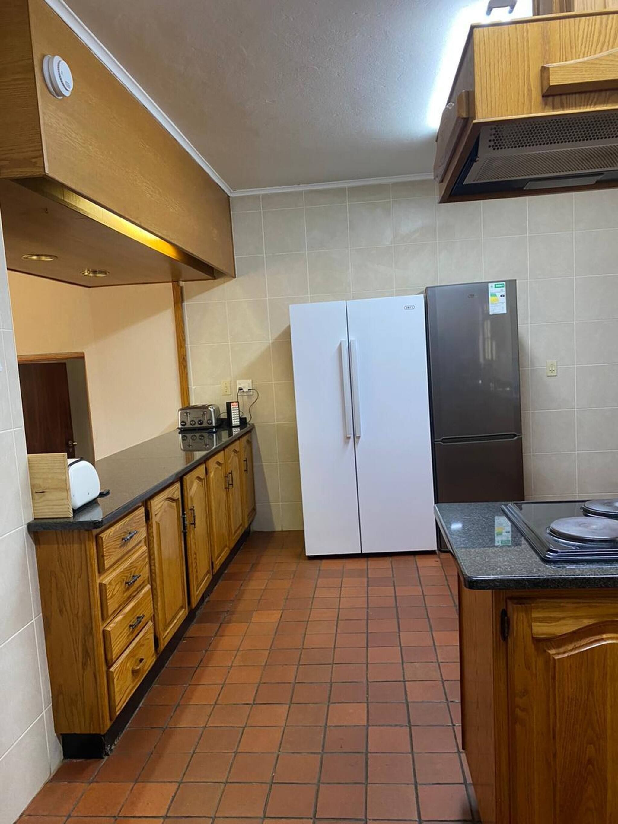 Una cocina con armarios de madera, un refrigerador blanco, un refrigerador negro, una estufa y un tostador.