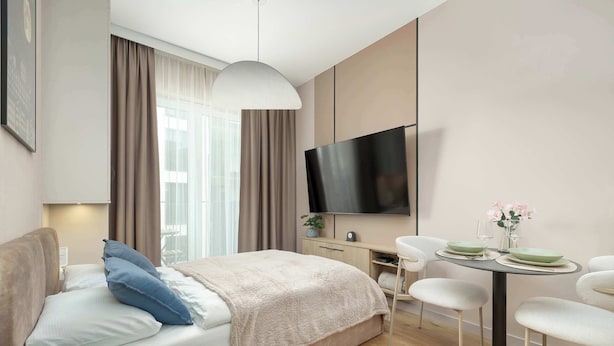 A modern hotel room with a bed, a desk, a TV, and a dining area. - Beige Apartment By the River | 2 Balconies (Szczecin)