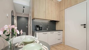 A modern kitchen with a black marble countertop, wooden cabinets, and a dining area with a round table set for two. - Beige Apartment By the River | 2 Balconies (Szczecin)