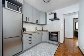 A modern kitchen with grey cabinets, a built-in microwave, a stainless steel refrigerator, and a patterned floor. - Spacious Apartment in Center | Balcony | Desk (Wrocław)