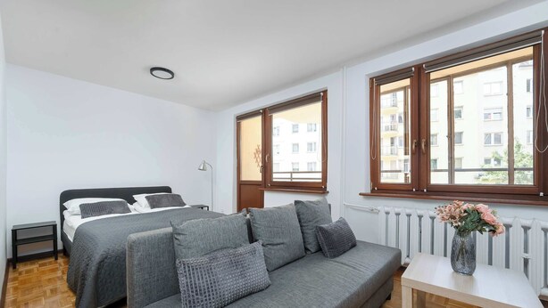 Ein Schlafzimmer mit einem Bett, zwei Sofas, einem kleinen Tisch und großen Fenstern.