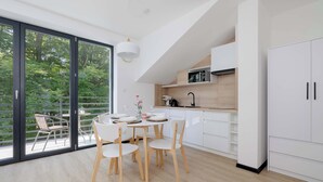 Une cuisine moderne avec des meubles blancs, un coin repas avec une table ronde et des chaises, et une grande porte-fenêtre coulissante donnant sur un espace extérieur.