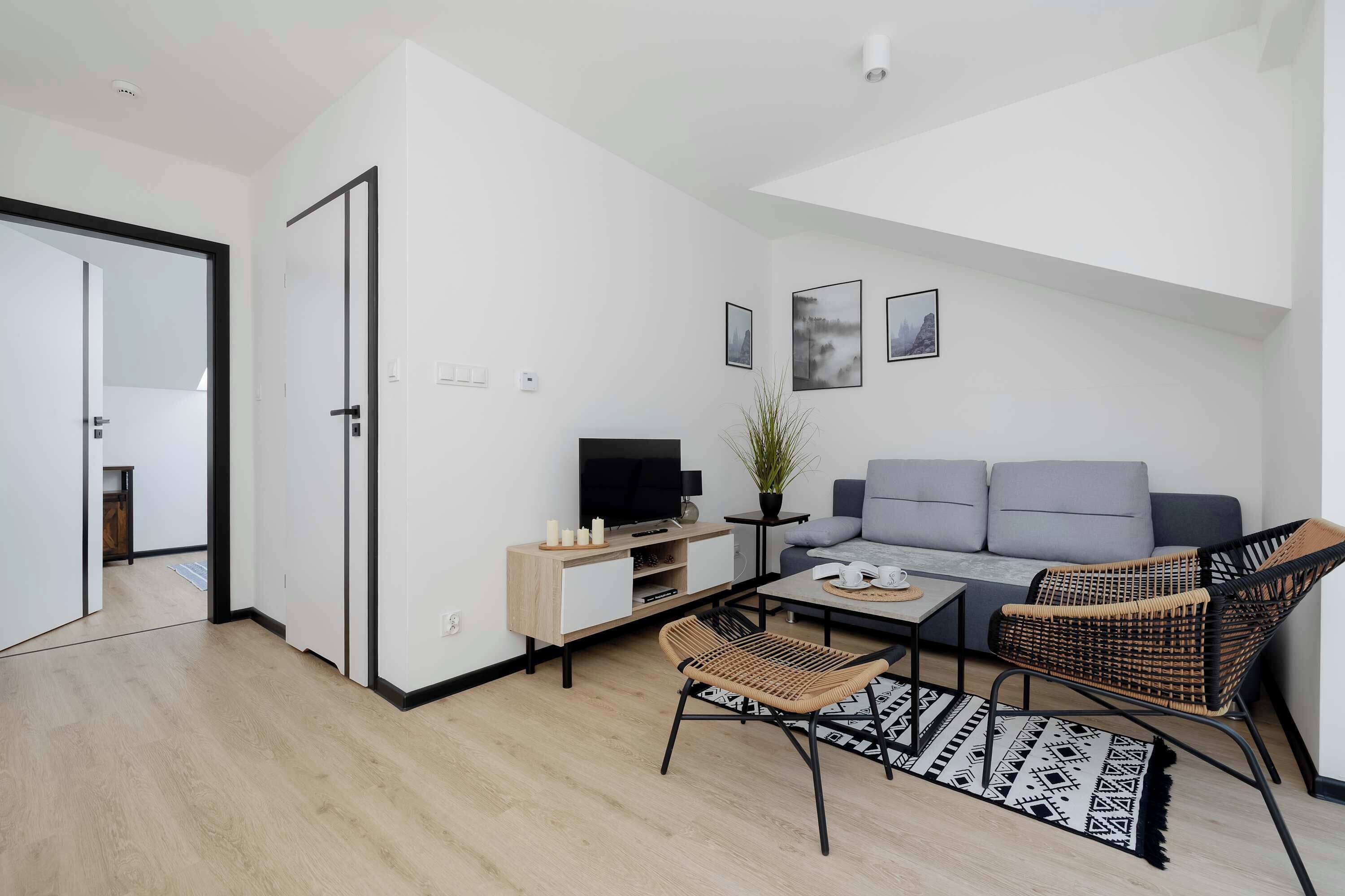 A modern living room with a sofa, a television, a coffee table, a wicker chair, and a patterned rug.
