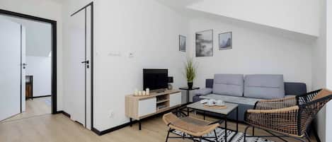 A modern living room with a sofa, a television, a coffee table, a wicker chair, and a patterned rug.