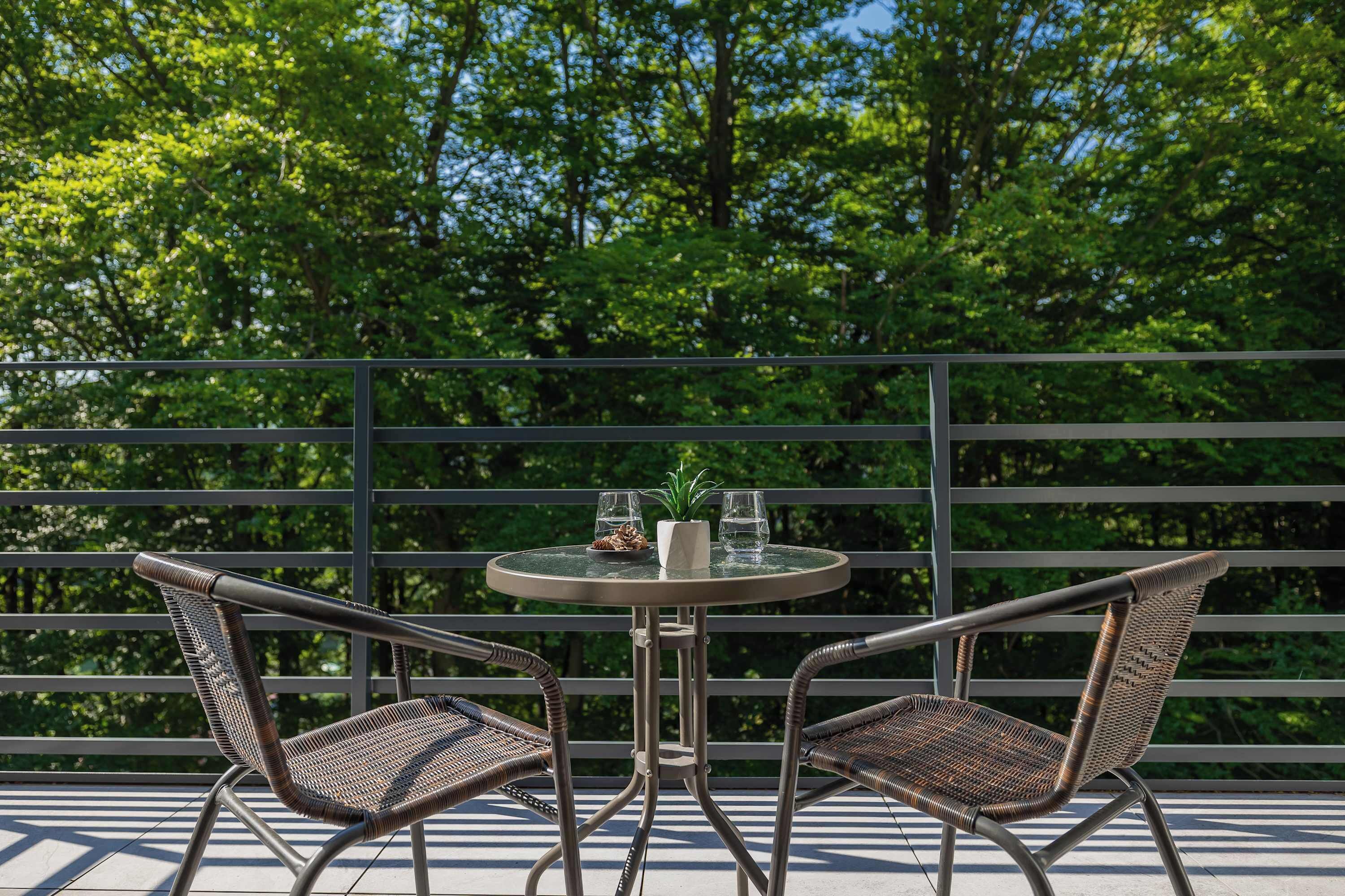 En balkon med to fletstole, et lille bord og en potteplante.