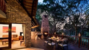 An outdoor deck with a brick fireplace, dining table, and chairs.