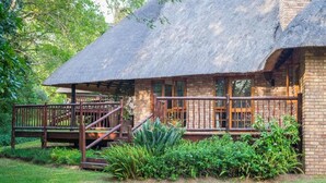 A rustic lodge with a thatched roof, wooden deck, and brick walls.