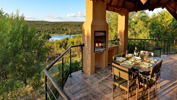 Un espace extérieur aménagé pour les repas, avec un barbecue, et offrant une vue panoramique sur un lac et une forêt.