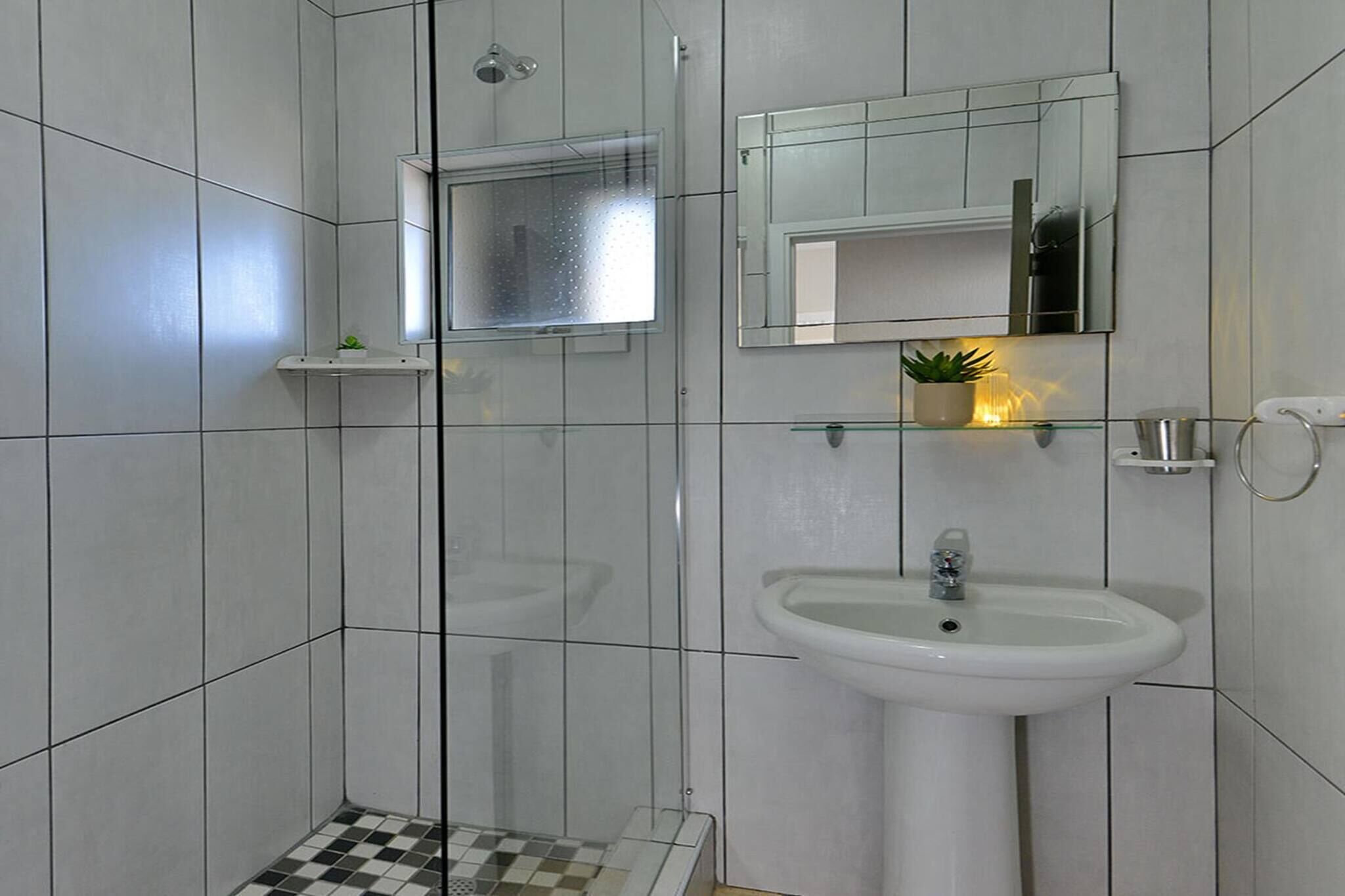Ein Badezimmer mit Dusche, Waschbecken, Spiegel und einem kleinen Ablagefach mit einer Pflanze.