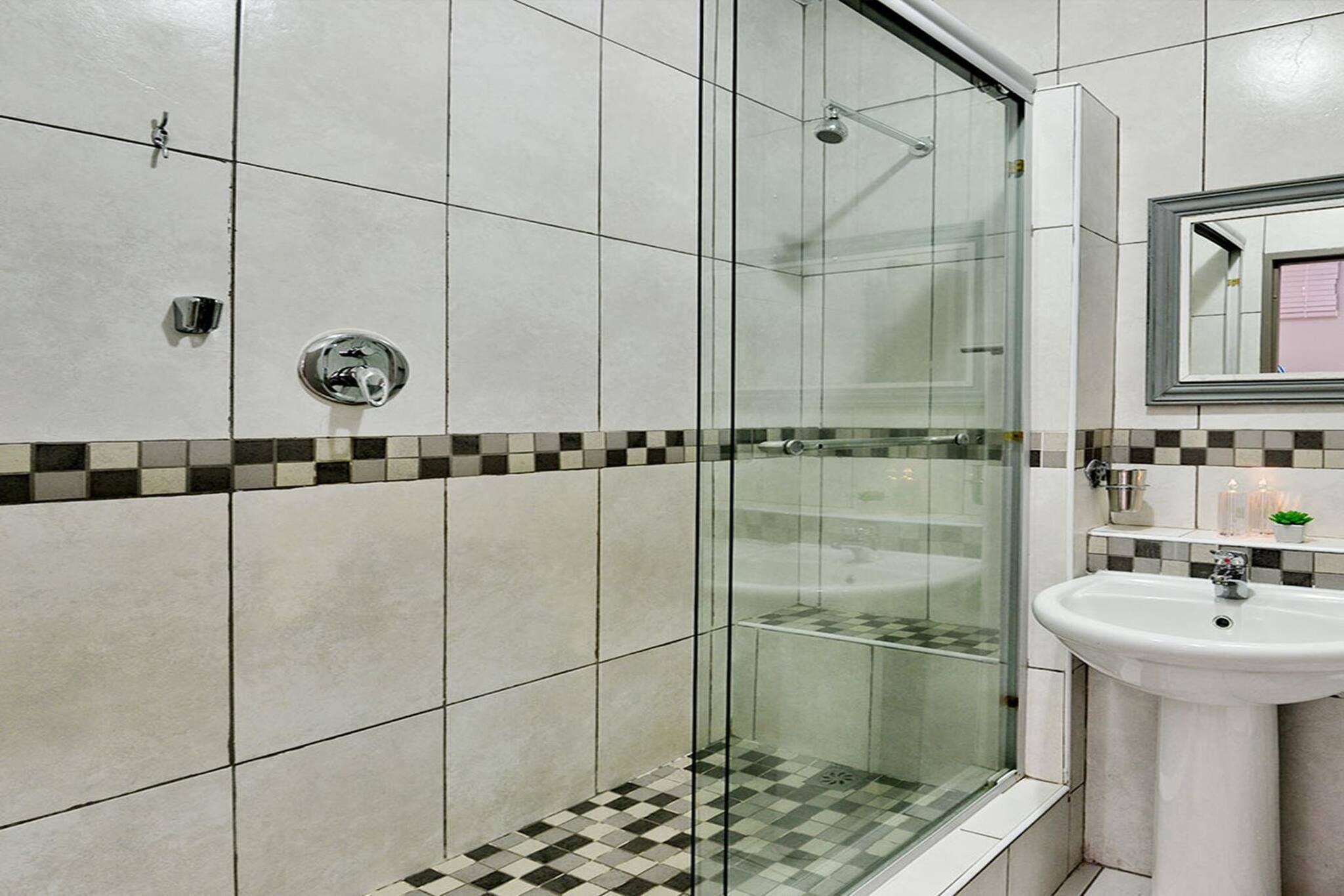 A bathroom with a glass-enclosed shower, a sink, and a mirror.