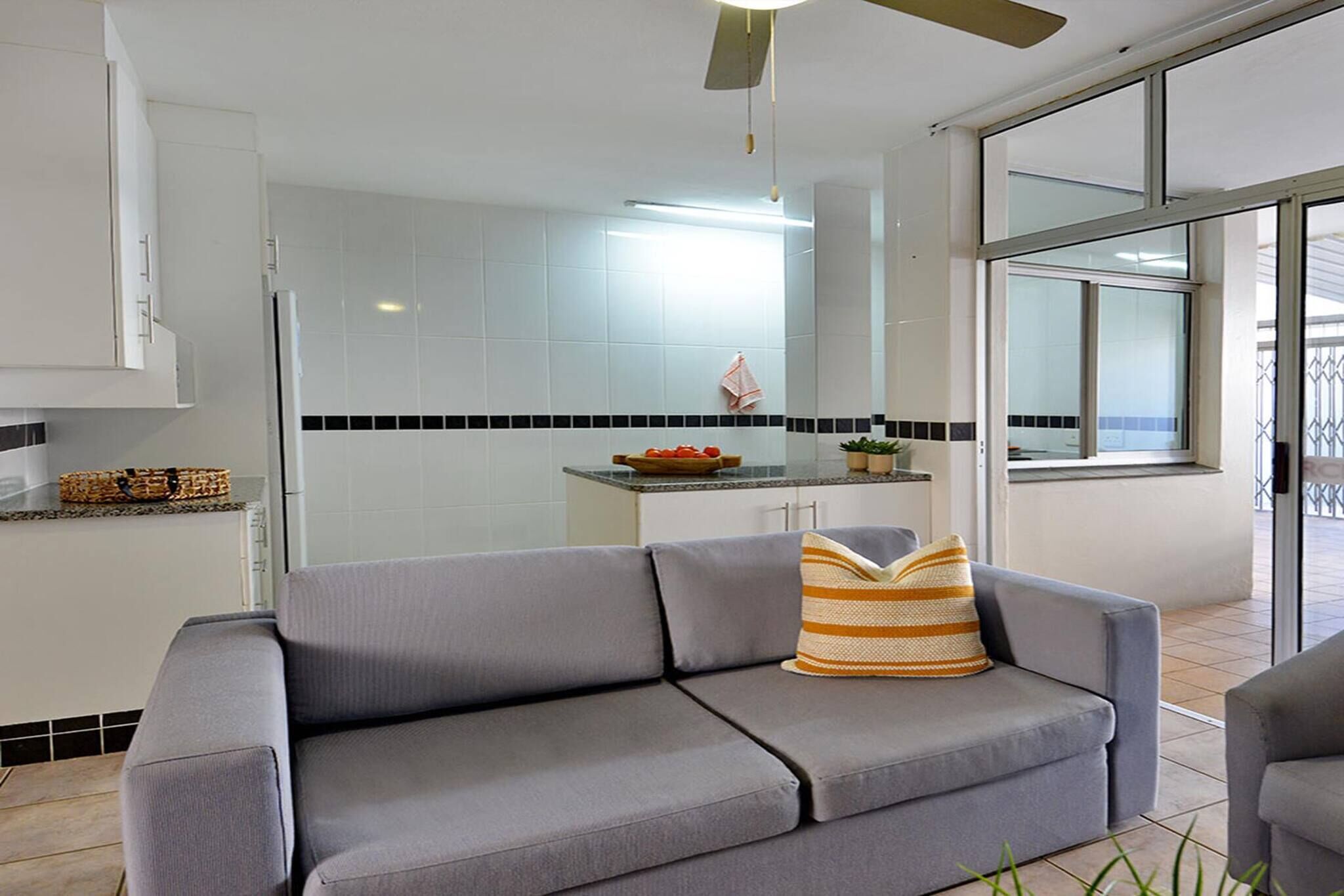 Una cocina moderna con armarios blancos, salpicadero blanco y negro, y puerta de vidrio que da a un balcón.