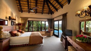 Un dormitorio con cama, televisor, escritorio, silla y balcón con vistas.