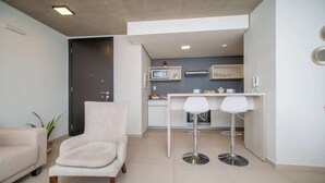 A modern living room with a sofa, a chair, and a small table. There is a kitchenette with a microwave and a coffee machine. - Corporate Stays Insignia 4 - A51 (Lúke)