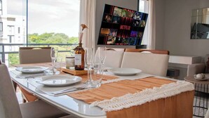 A dining area with a table set for four, a TV displaying Netflix content, and a view of greenery outside. - Corporate Stays Insignia 4 - A51 (Lúke)