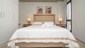 A neatly made bed with a white and brown striped bedspread, two bedside lamps, and two framed artworks on the wall. - Corporate Stays Insignia 4 - A51 (Lúke)