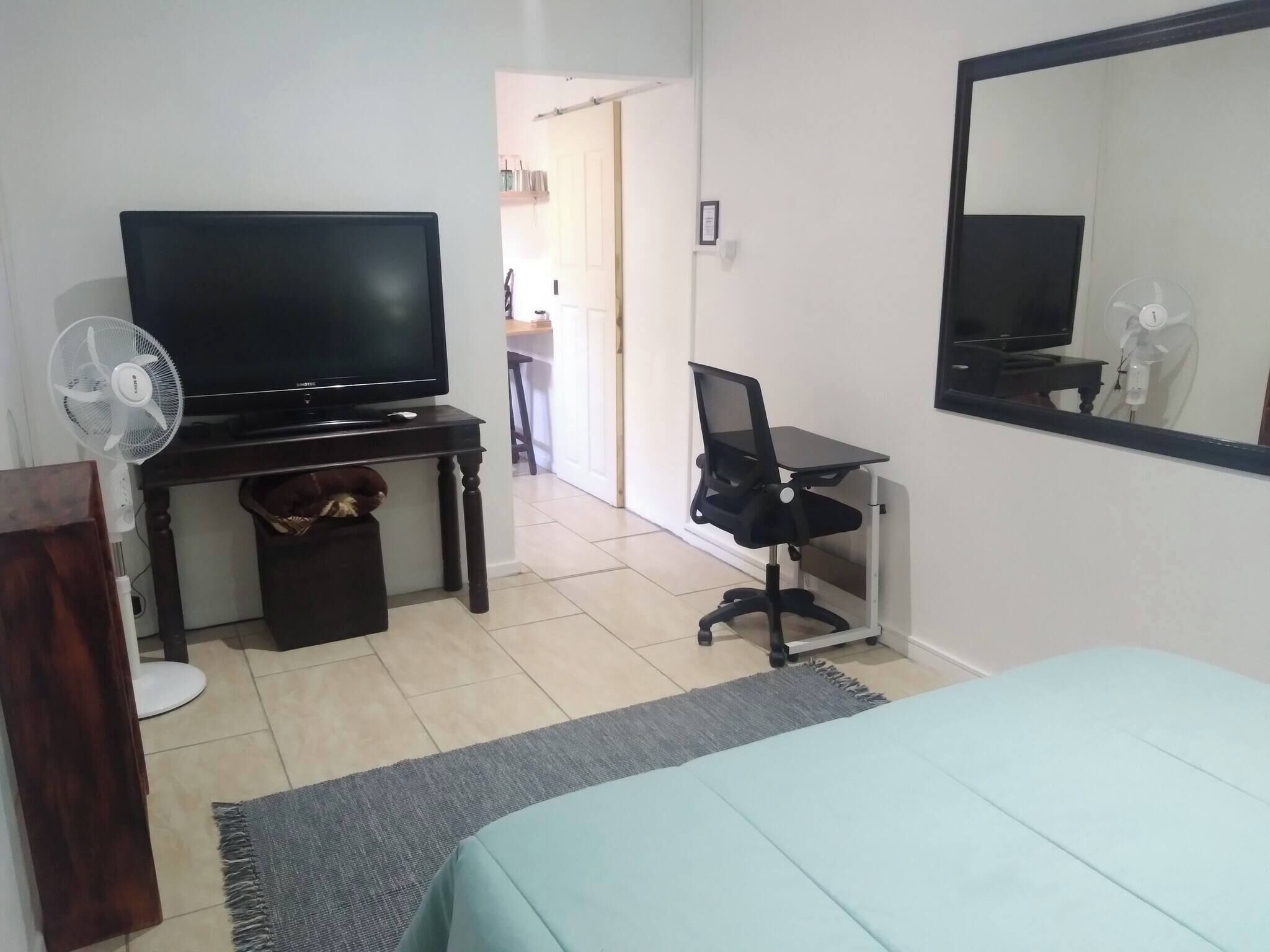 Une chambre avec un lit, un bureau avec une chaise, une télévision et un ventilateur.