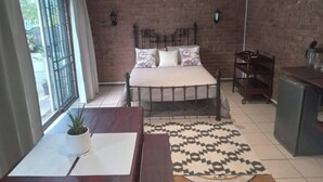 Une chambre à coucher avec un lit, un bureau, une chaise, une plante en pot, un tapis à motifs et un mur en briques.