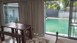Une pièce comprenant une table à manger, des chaises, un tapis à motifs, une porte-fenêtre coulissante et une vue sur une piscine.