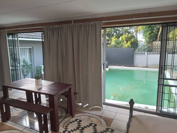 A room with a dining table, chairs, a patterned rug, a sliding glass door, and a view of a swimming pool.