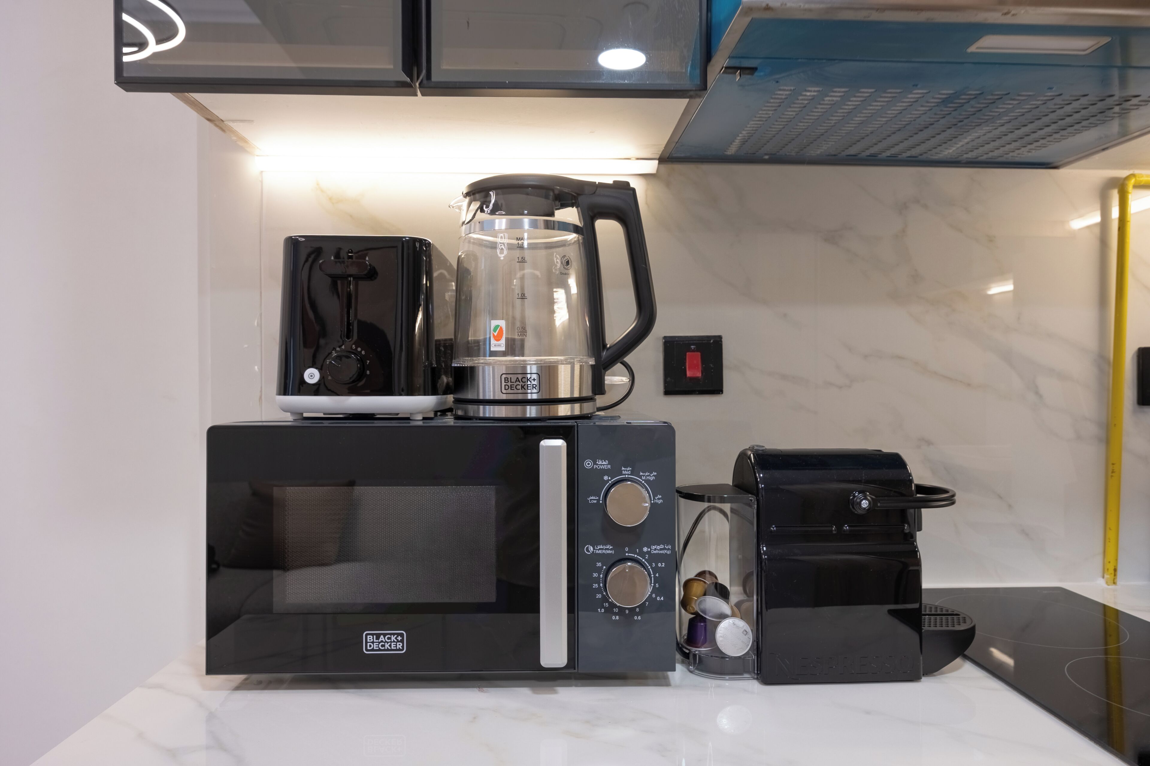 Una cocina con un microondas negro, una cafetera y un hervidor sobre la encimera.
