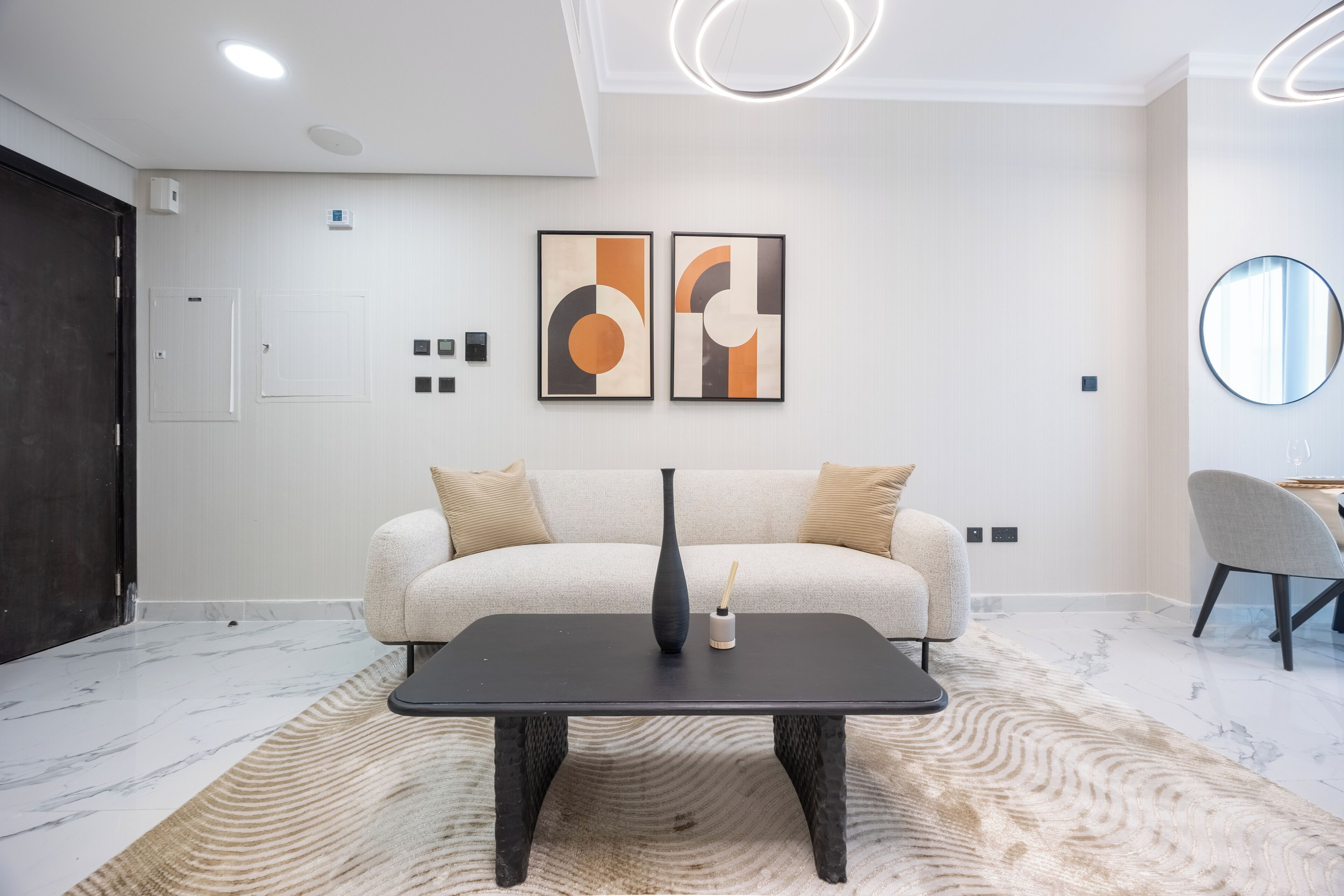 Un salon moderne avec un canapé, une table basse, des œuvres d’art abstraites, un miroir et une porte.