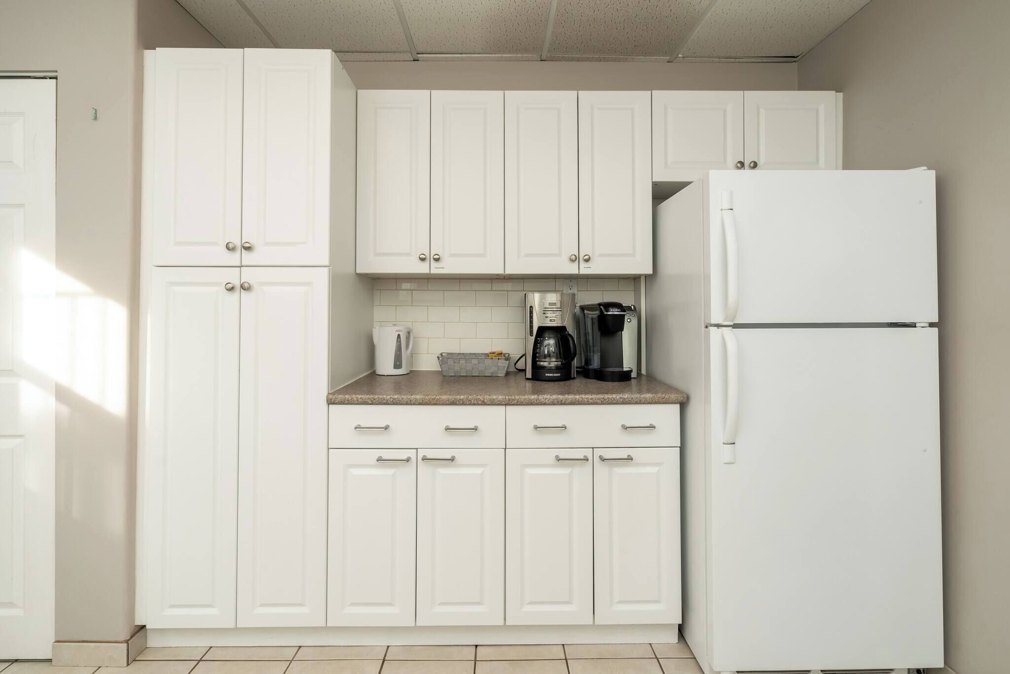 A kitchen with white cabinets, a refrigerator, and a coffee maker on the counter.