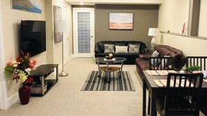 Un salon comprenant un canapé, une table basse, un téléviseur, une table à manger avec des chaises, et une porte avec du verre dépoli.