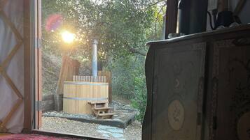 Une pièce dotée d’une grande porte-fenêtre coulissante qui donne sur un espace extérieur agrémenté d’une structure en bois et d’une cheminée. Le sol est recouvert d’un tapis à motifs et la pièce contient un meuble au design décoratif.