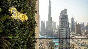 A view of a cityscape with prominent skyscrapers, including the Burj Khalifa and Emaar Tower, through a window with a 'Google' sign on the left. - Luxury 3.5BR Burj Khalifa LED View  (Dubai)