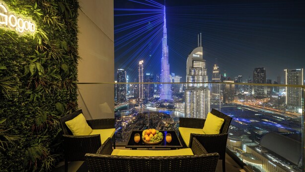 A balcony with a cityscape view, a table with fruit, and a wall with greenery. - Luxury 3.5BR Burj Khalifa LED View  (Dubai)